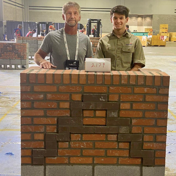  student and teacher stand behind a brick wall